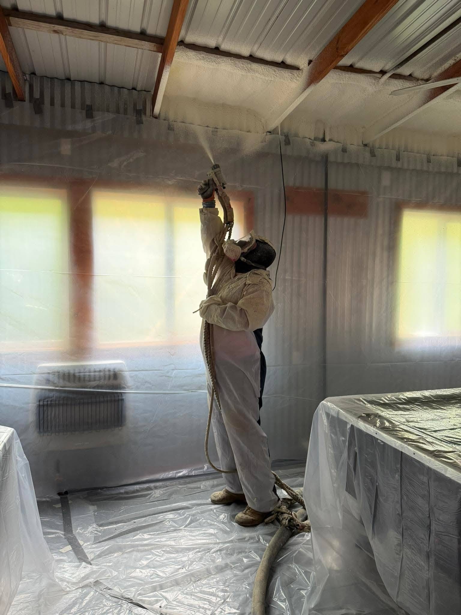 Installer in full protective gear spraying foam insulation on a ceiling