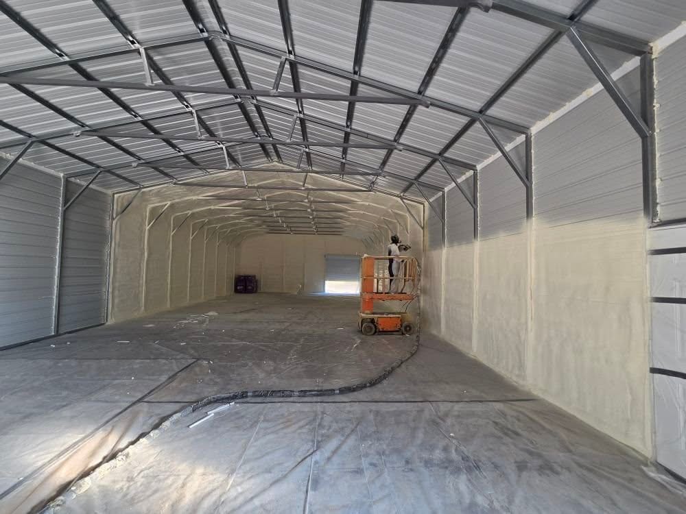 Spray foam being applied to the walls of a long metal building from a lift